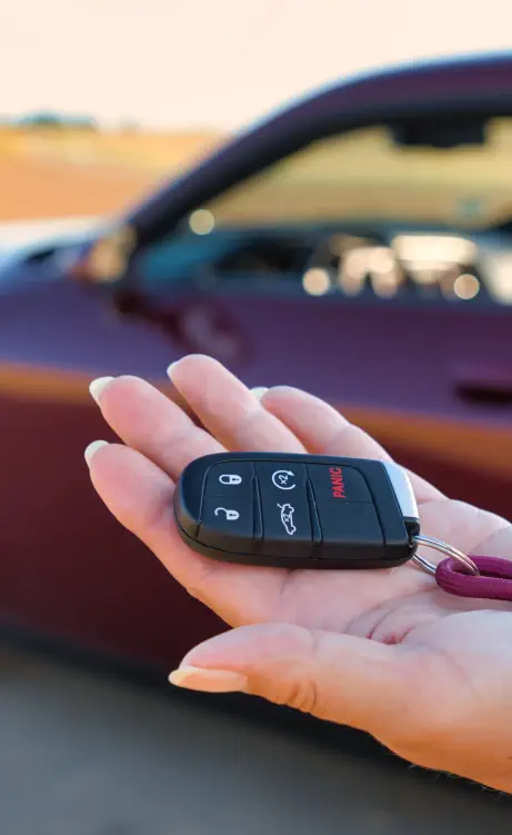 Secure 16-year veteran vehicle delivery with keys in hand and a maroon Doge Challenger.