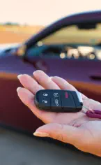 Secure 16-year veteran vehicle delivery with keys in hand and a maroon Doge Challenger.